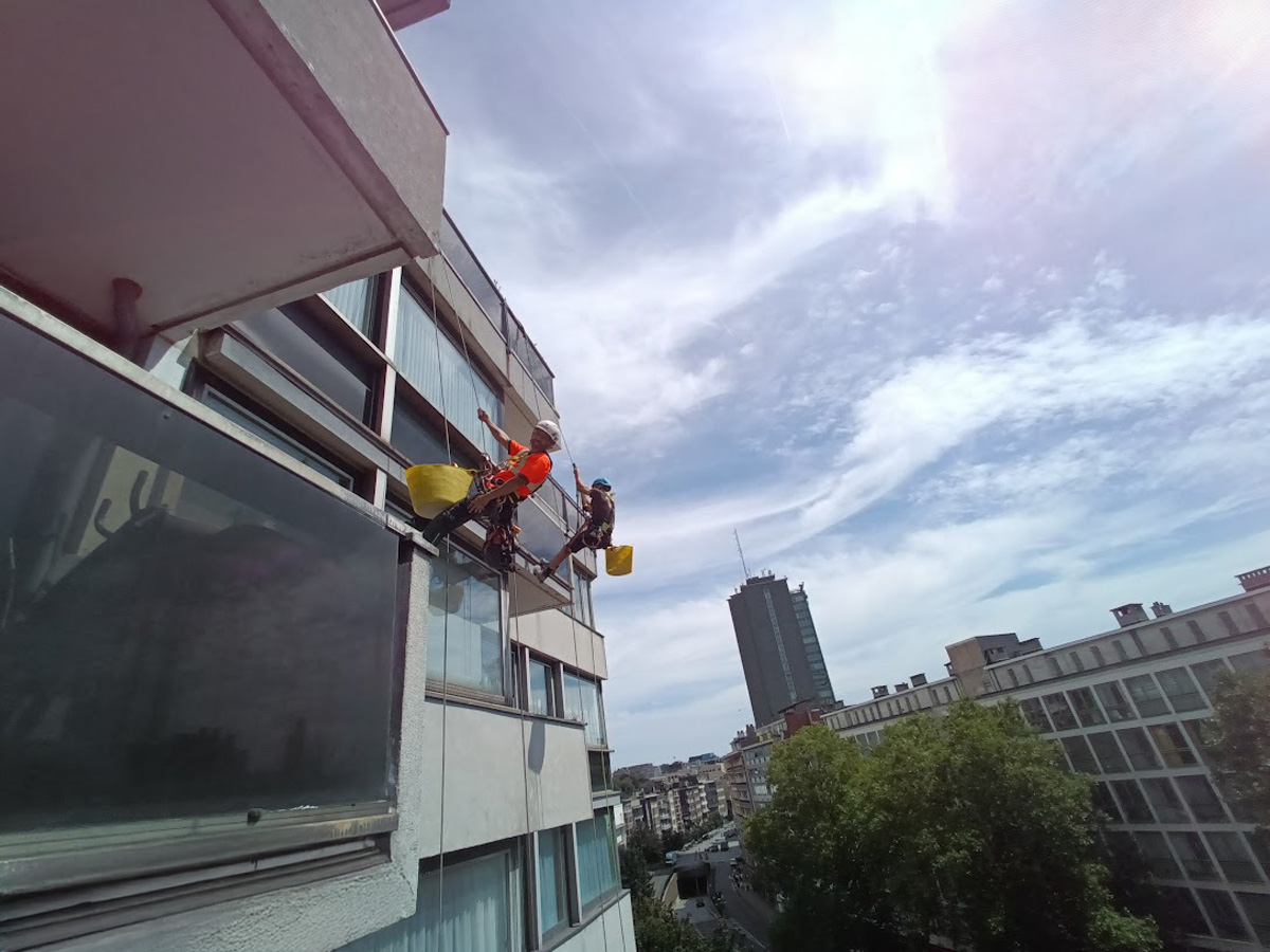 Cordiste Vertikal Pro effectuant le nettoyage de vitres en rappel sur une façade moderne de grande hauteur.