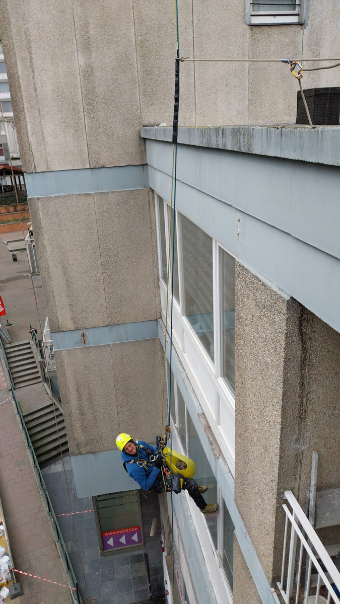 Cordiste professionnel en rappel effectuant le nettoyage de vitres de bureau difficile d'accès sur une façade moderne.