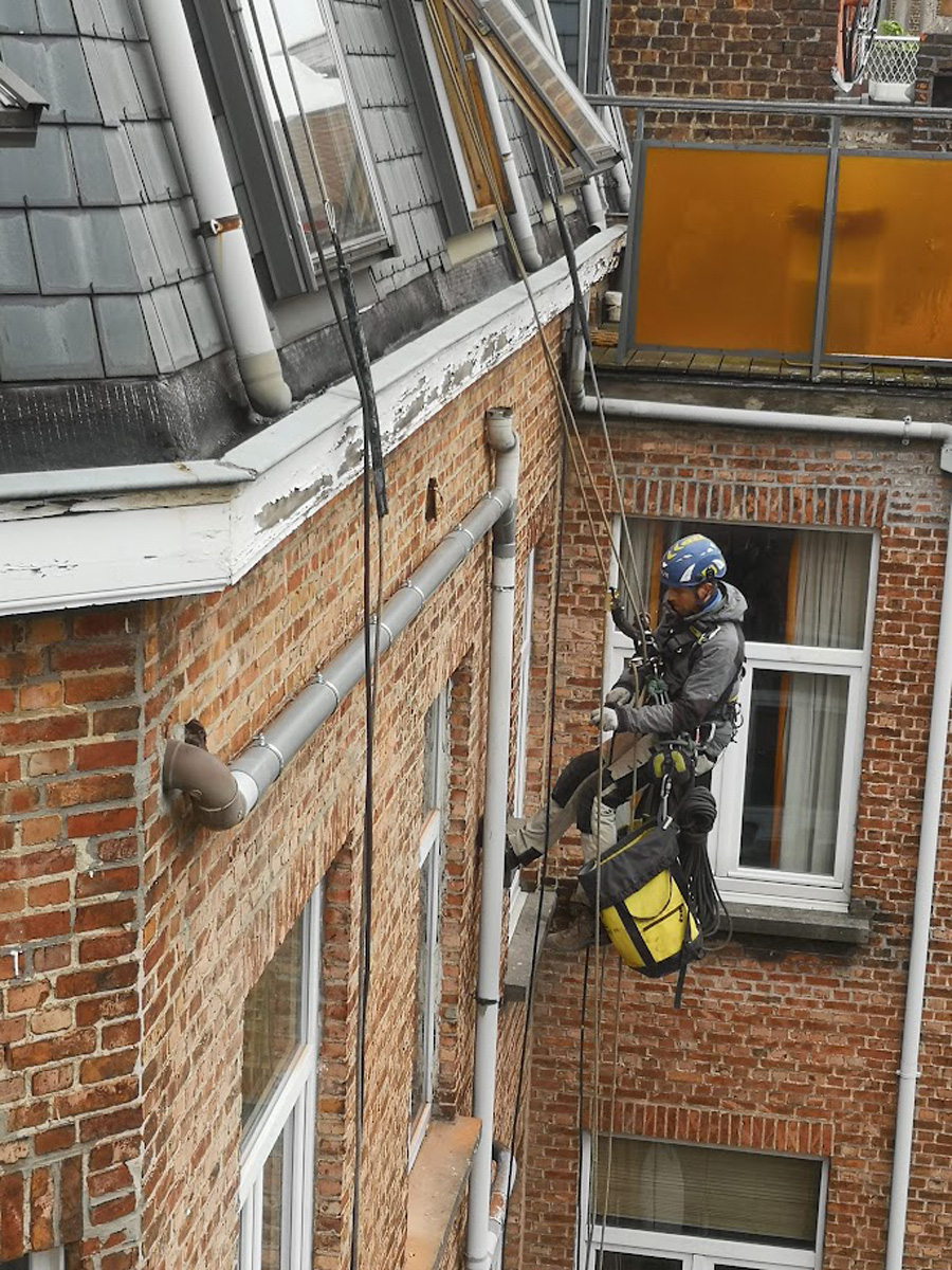 Expert cordiste réparant une maçonnerie de façade en briques près d'une fenêtre et d'une corniche à Bruxelles.