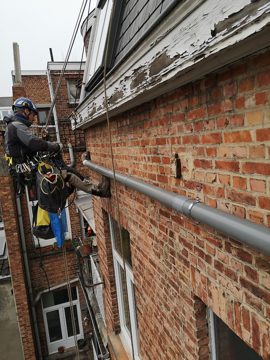 Installation et fixation technique d'une descente d'eau pluviale sur façade en rappel par l'équipe Vertikal Pro.